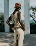 Woman in a beige outfit with a headscarf and sunglasses standing outdoors with ocean view.
