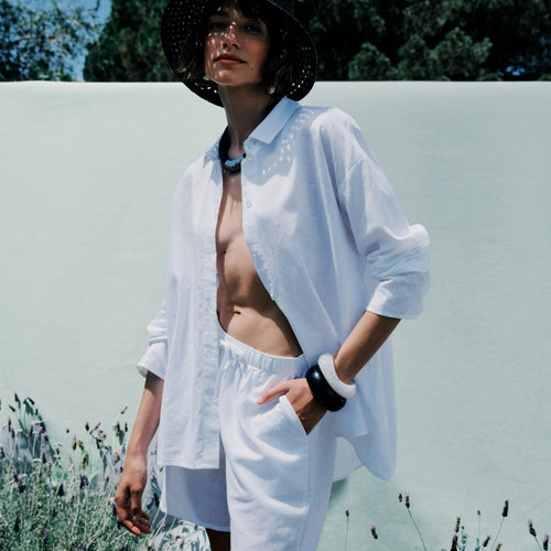 Woman in a white shirt and shorts standing outdoors with a blurred background