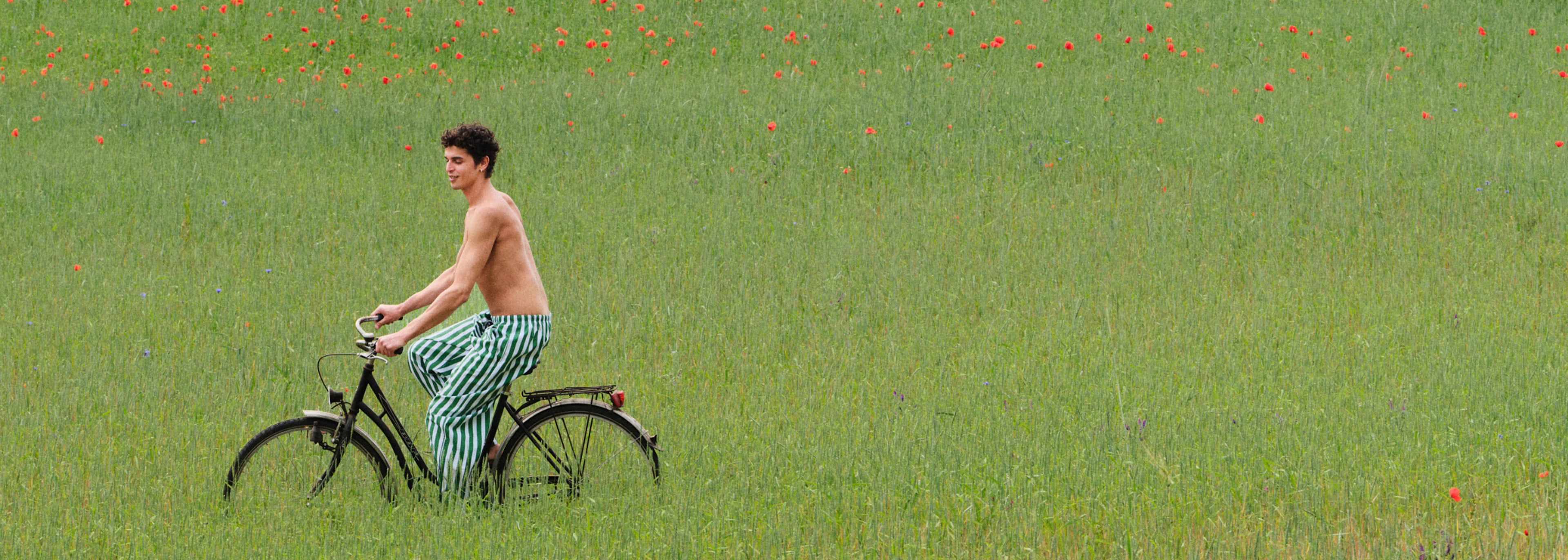 Man riding a bicycle in a field of green grass with red flowers