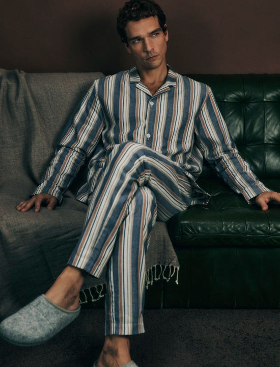 Man wearing a striped pajama set sitting on a couch.
