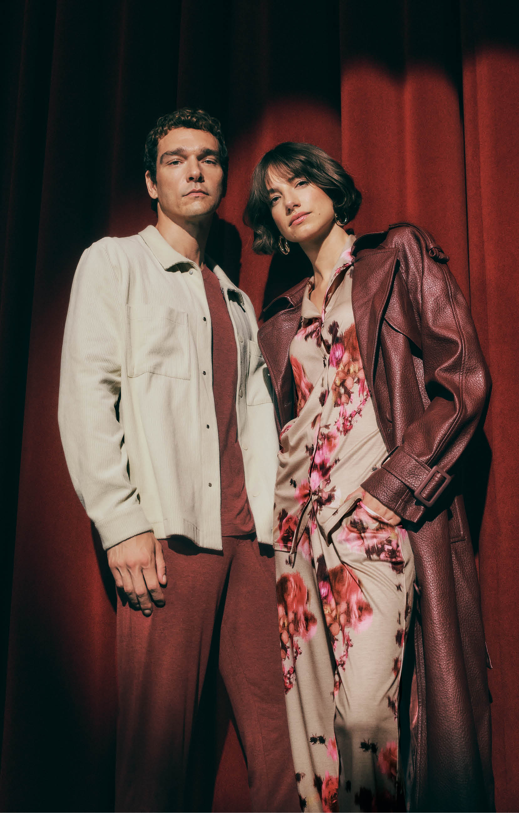 Two people standing against a red curtain backdrop. Wearing Casuals and Olivia