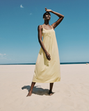 Woman in a yellow dress standing on a beach with a clear blue sky.