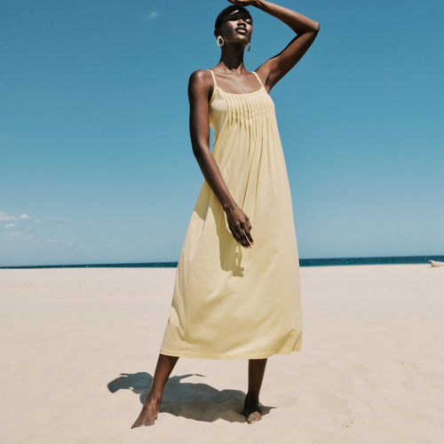 Woman in a yellow dress standing on a beach with a clear blue sky.