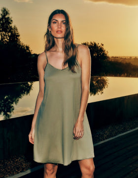 Woman in a green dress standing by a lake at sunset
