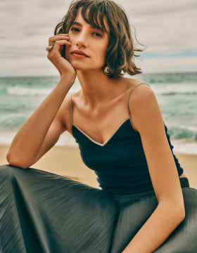 Woman sitting on a rock by the ocean wearing a deep navy top and long skirt